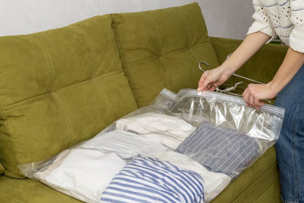 A woman packs summer clothing into a clear storage bag.