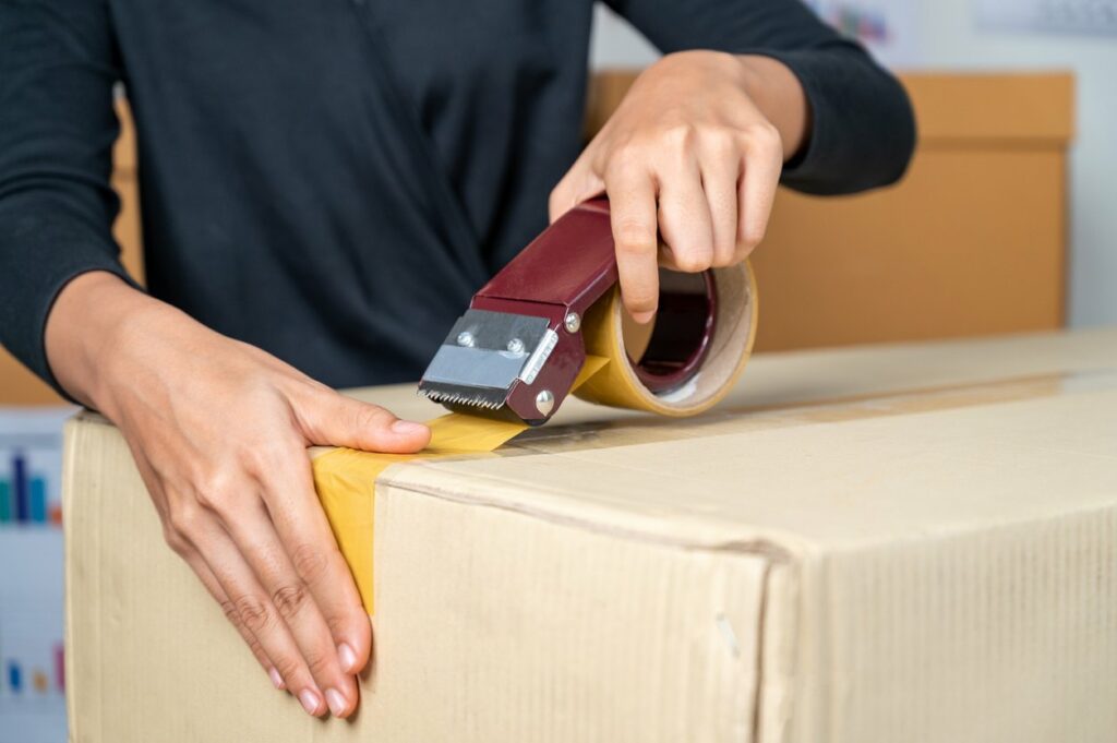 A person uses packing tap to close a cardboard box.