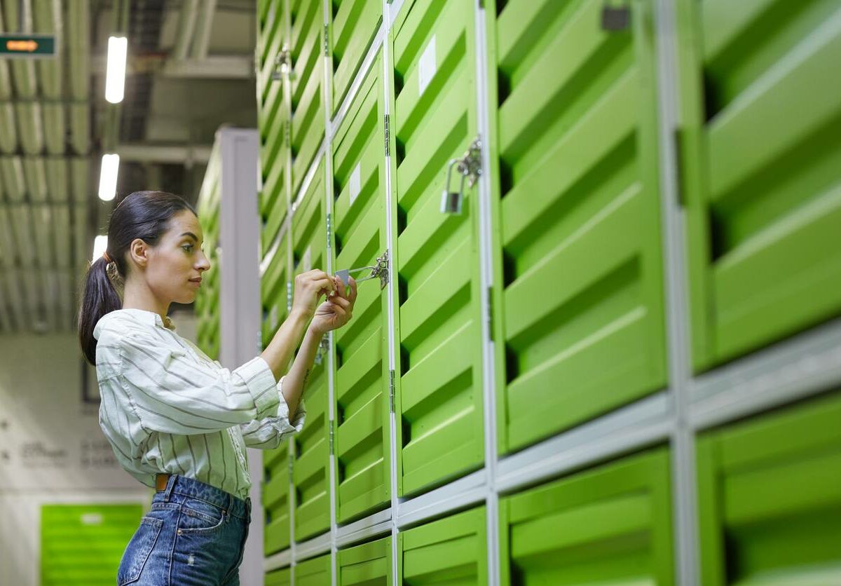 A woman stands in front of a green storage locker to unlock it.