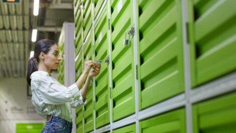 A woman stands in front of a green storage locker to unlock it.