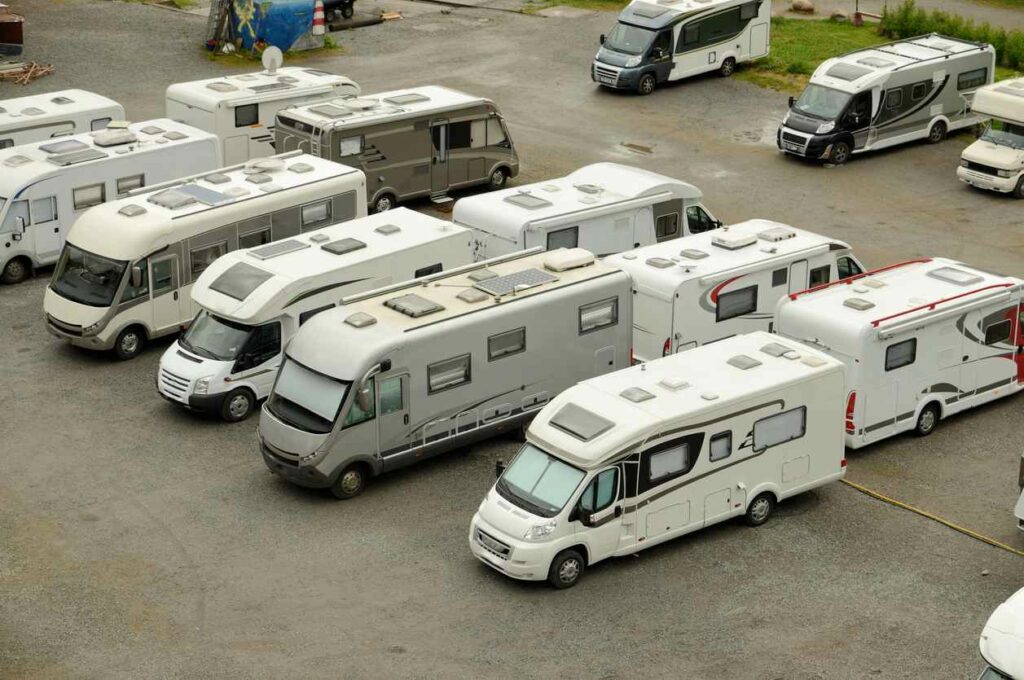 RVs are parked in a line in an uncovered, paved parking lot