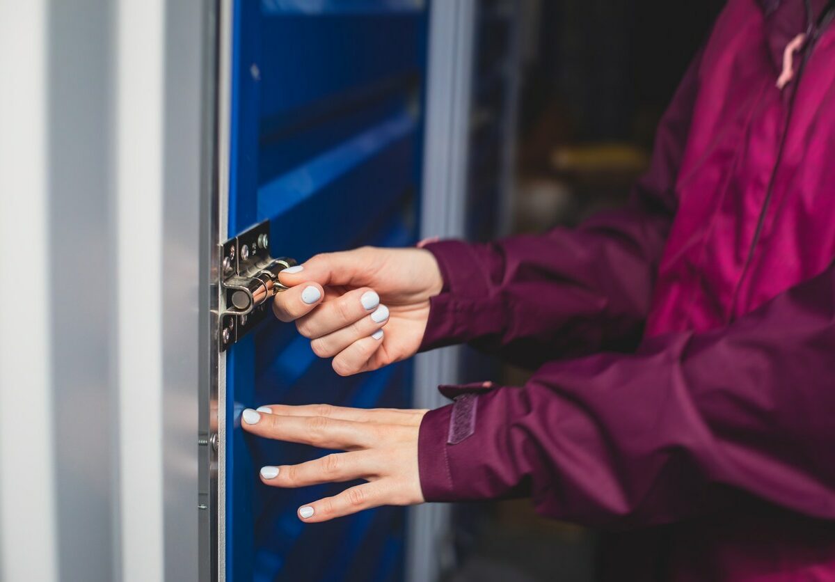 A woman wearing a pink coat unlocks and opens a storage unit door.