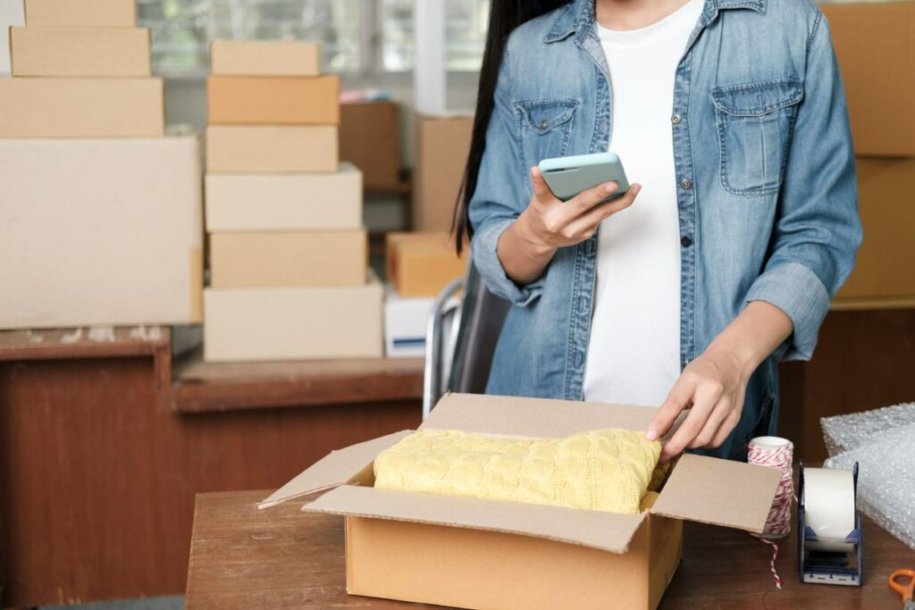 A woman searches on her phone while surrounded by small cardboard boxes