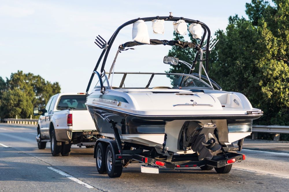 A pickup truck tows a boat on a trailer down the highway.