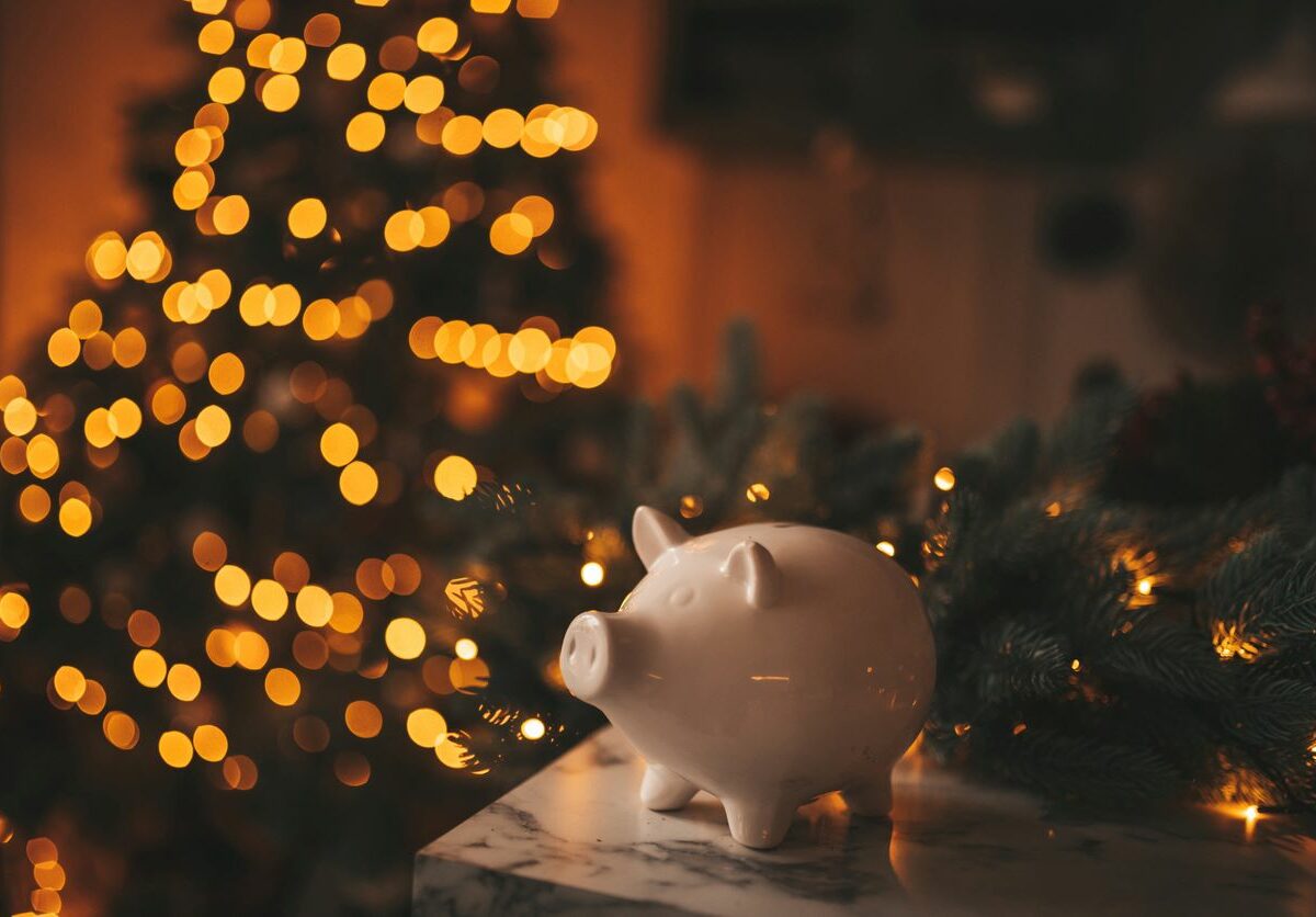 Piggy bank on countertop with Christmas tree and lights illuminated in the background.