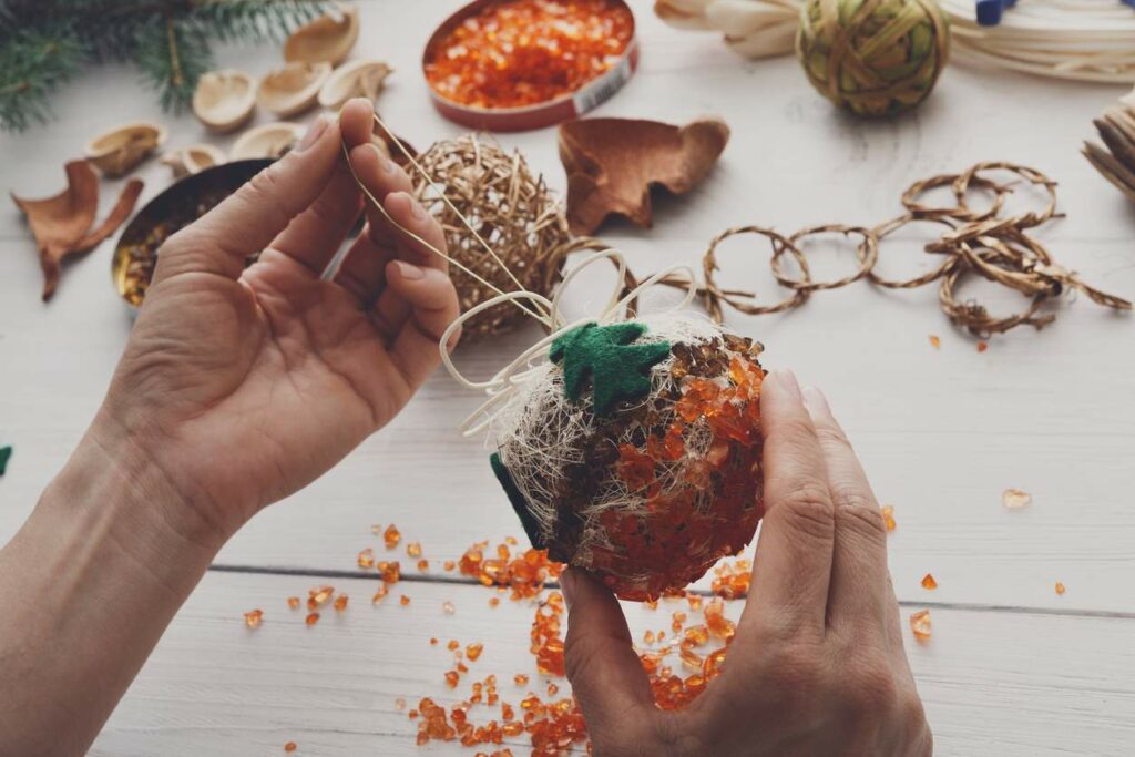 : Close-up shot of a person making their own Christmas ornament on a white wooden table.