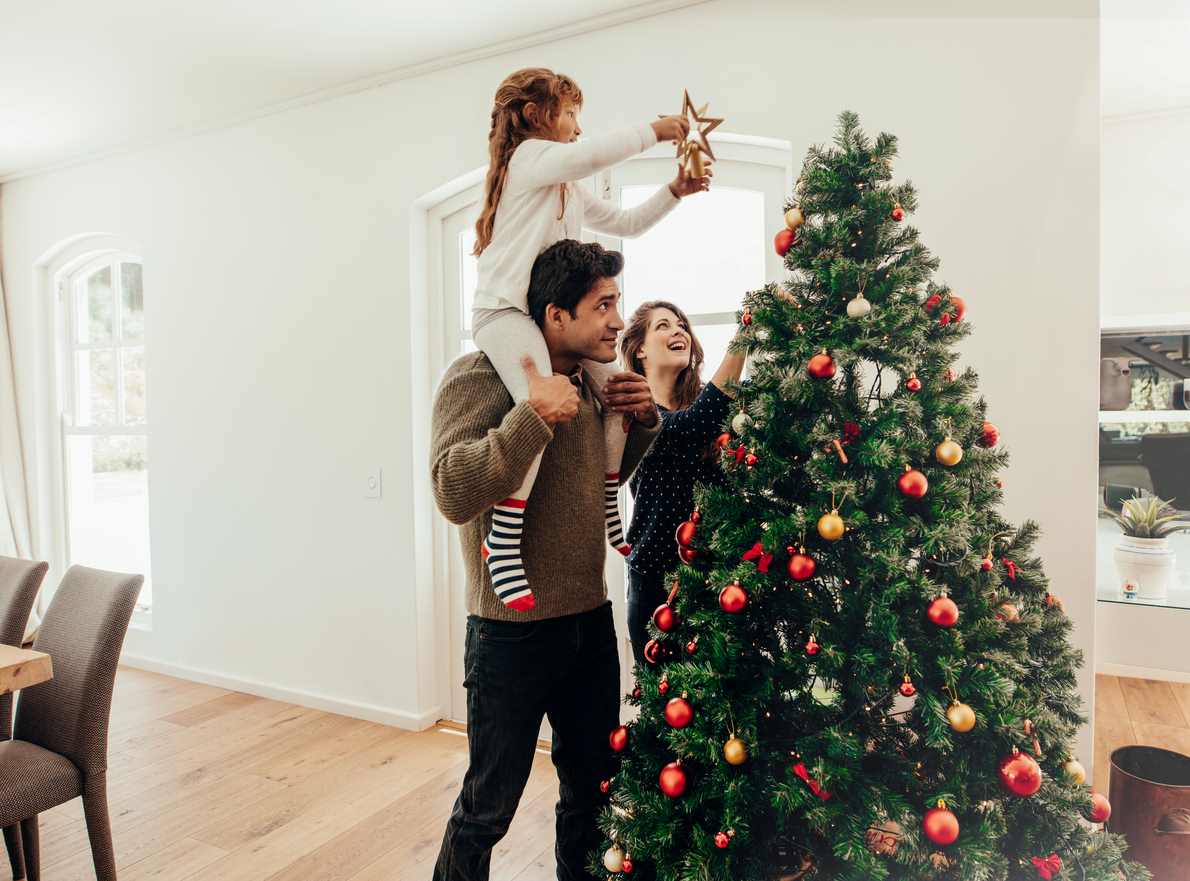 A woman holds her daughter as she puts the star on top of their artificial Christmas tree.