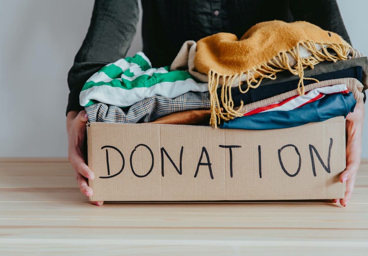 Woman holding a cardboard donation box full of folded clothes.