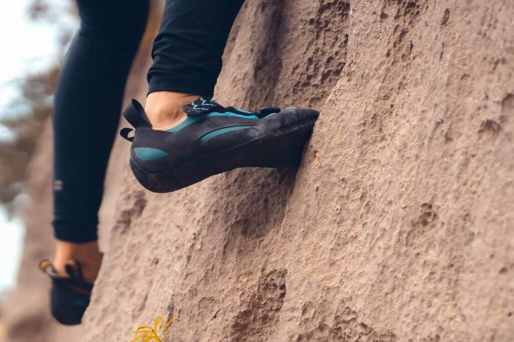 A close-up view of a person climbing a boulder in special climbing shoes.