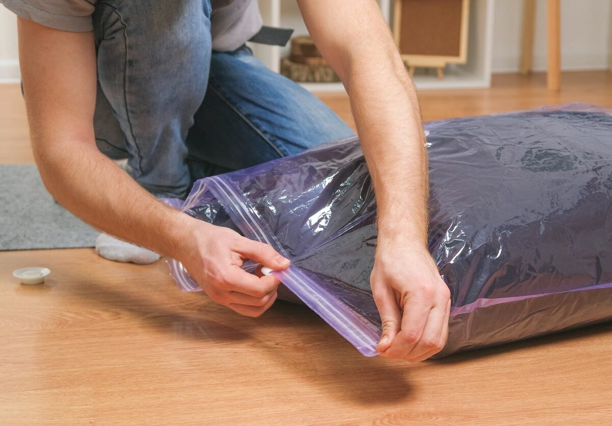 A man putting a winter jacket in a vacuum-sealed bag for storage.