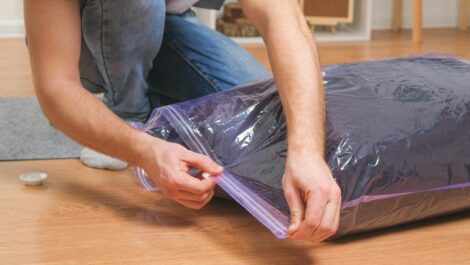 A man putting a winter jacket in a vacuum-sealed bag for storage.