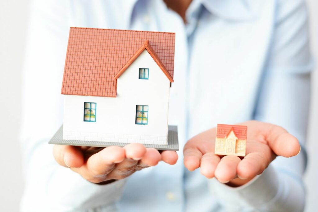 Two different sized toy homes held in hands to symbolize different homes to buy.