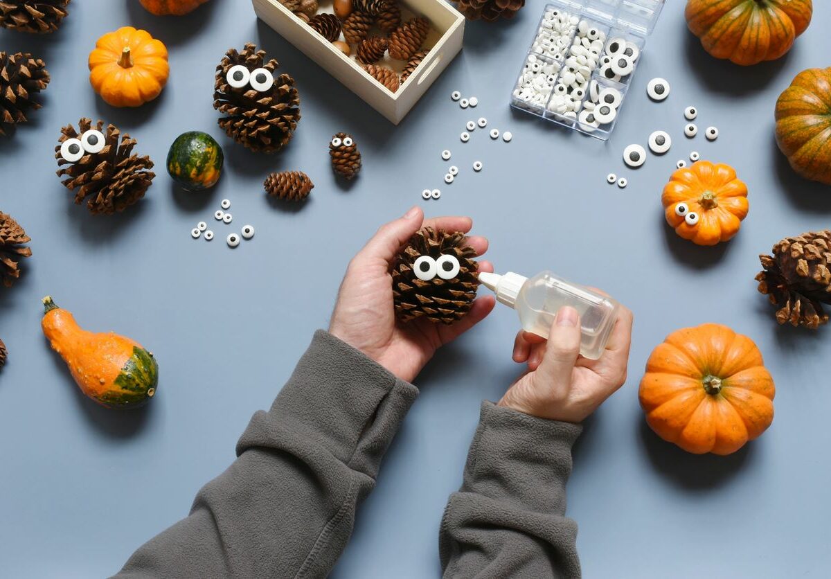 Making DIY fall decorations with pumpkins, pine cones, and glue-on eyes.