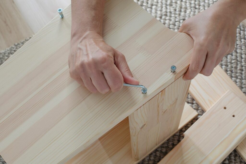 A person tightens a screw with an Allen wrench while assembling wooden furniture.