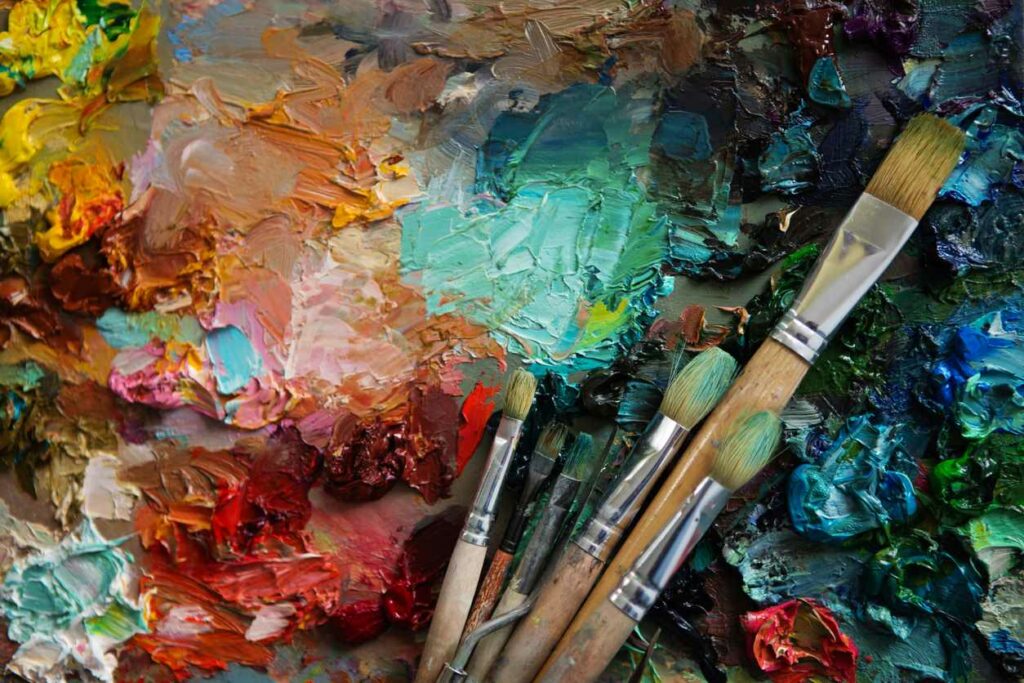 A group of paintbrushes lay on a canvas of thick, colorful paint.