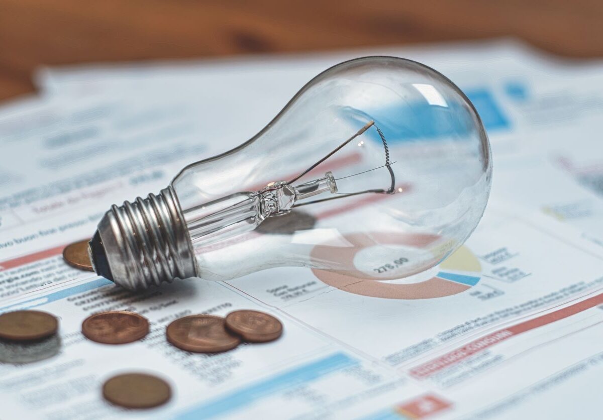 An incandescent light bulb sits next to several pennies on a power bill.