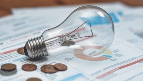 An incandescent light bulb sits next to several pennies on a power bill.