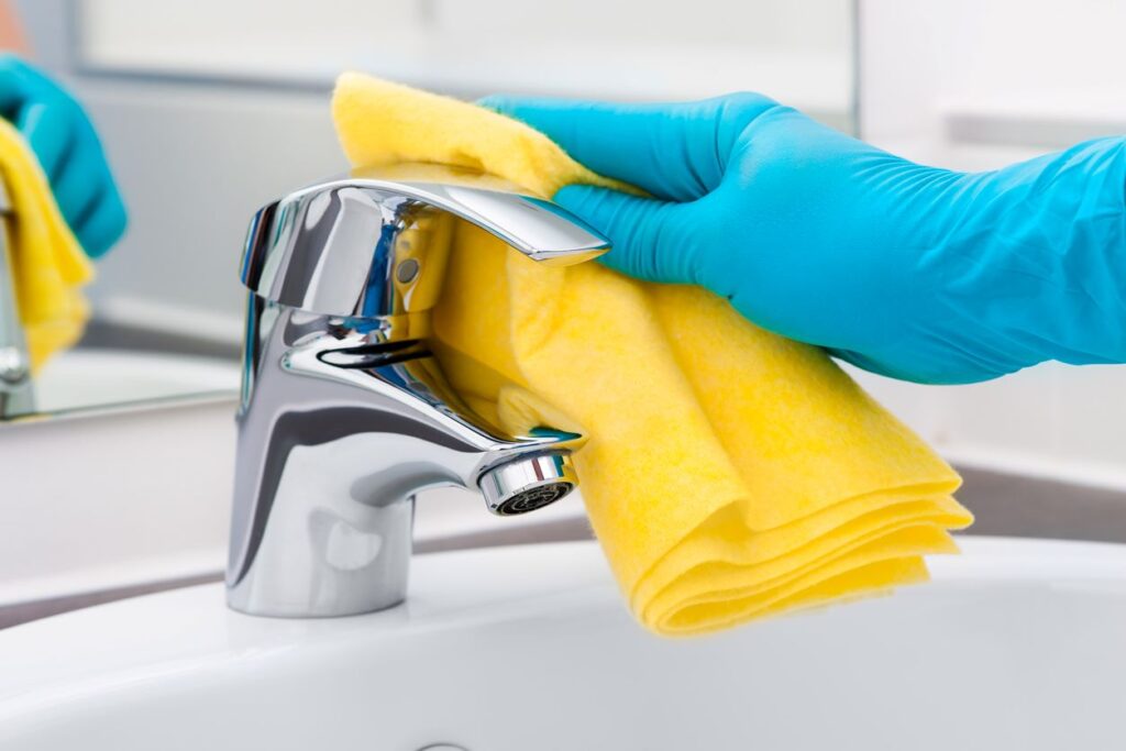 A gloved hand wipes down a metal sink faucet.