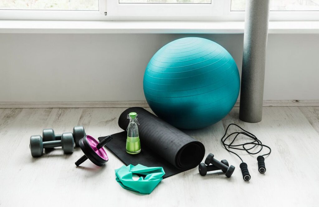 A yoga ball, mat, free weights, and jump rope sitting by a wall.