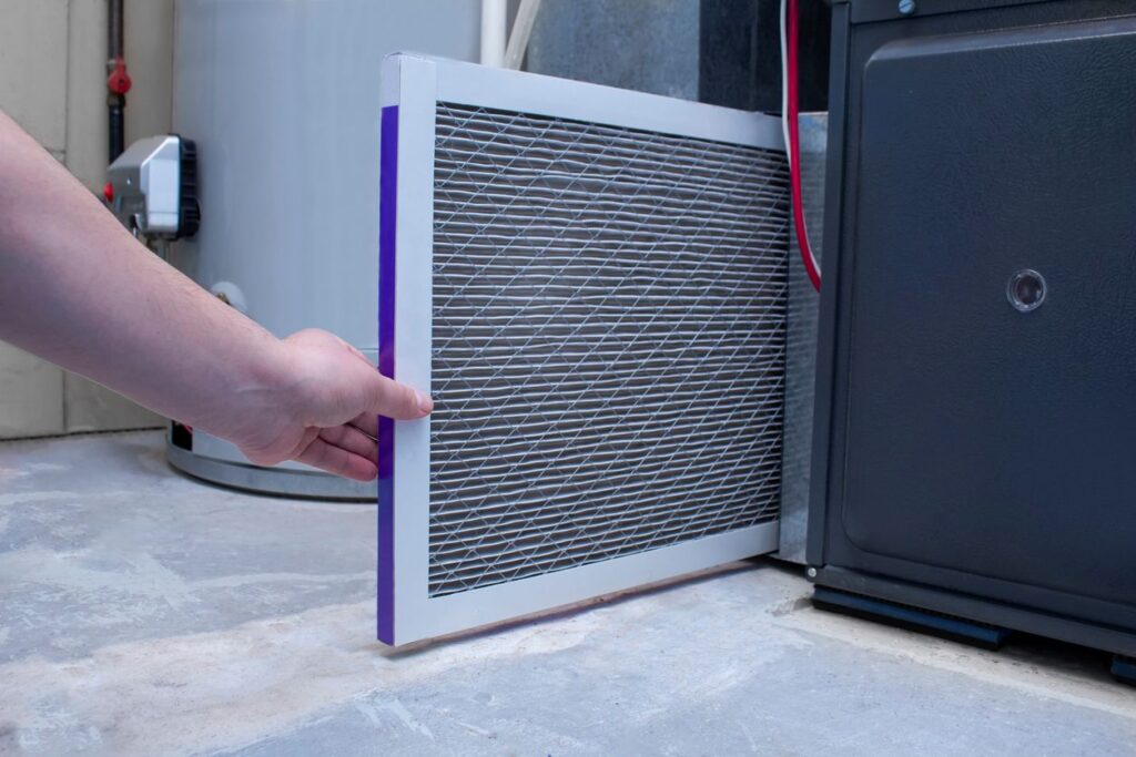 A person replaces their HVAC air filter by the furnace.