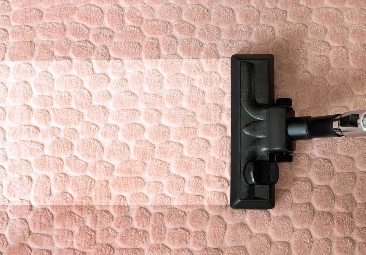 A vacuum cleans dirt from a tan-colored rug.